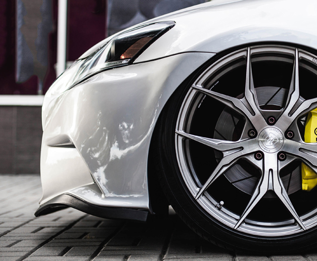 Close-up photo of a fender and wheel on a lowered white Lexus tuner with large custom rims and low profile tires.